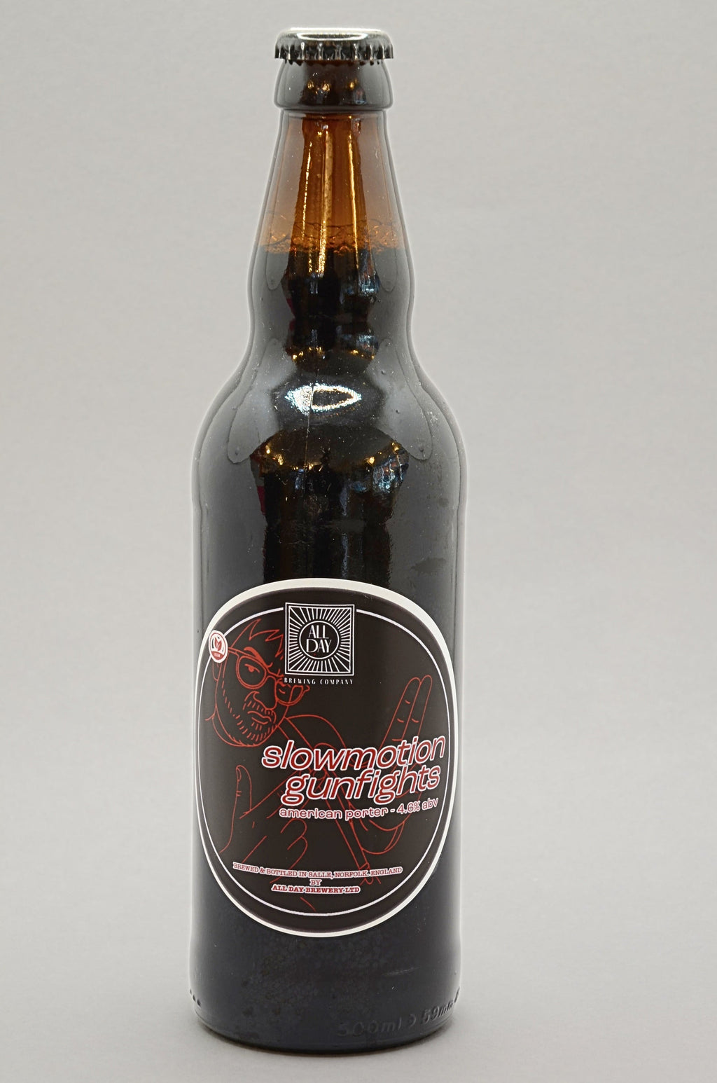 A dark brown glass bottle of All Day Brewing beer with a black cap and a black label featuring red and white text, set against a plain light gray background.